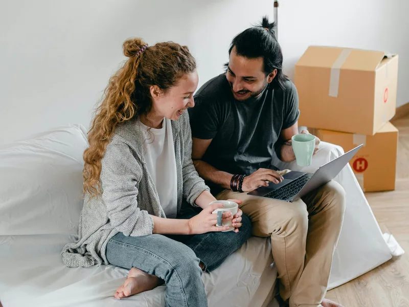 Pareja en un sofá con una computadora portátil junto a cajas de mudanza