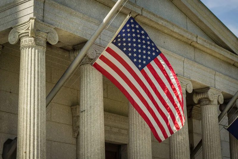Bandera estadounidense frente a un edificio con columnas de piedra.