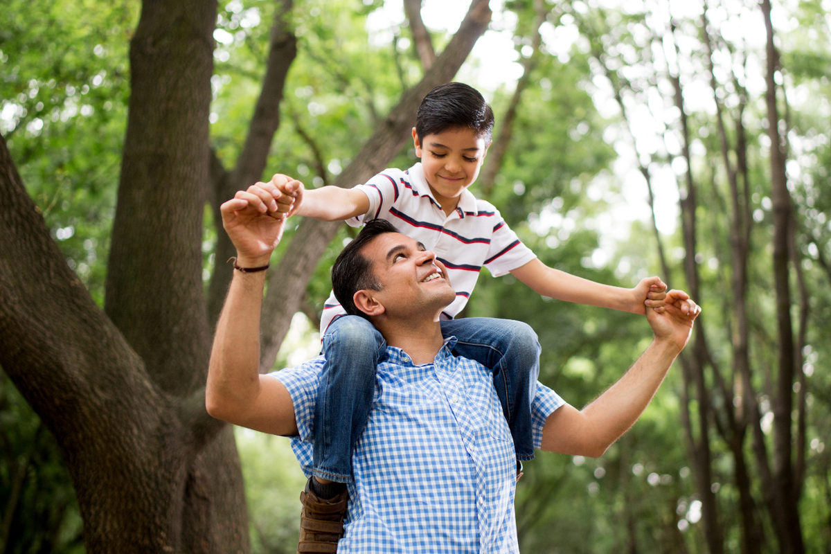 A man carrying a child on his shoulders among trees.