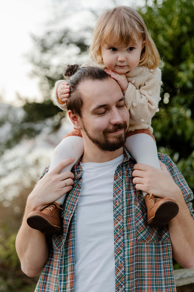 Padre cargando sobre los hombros a su hija sonriente