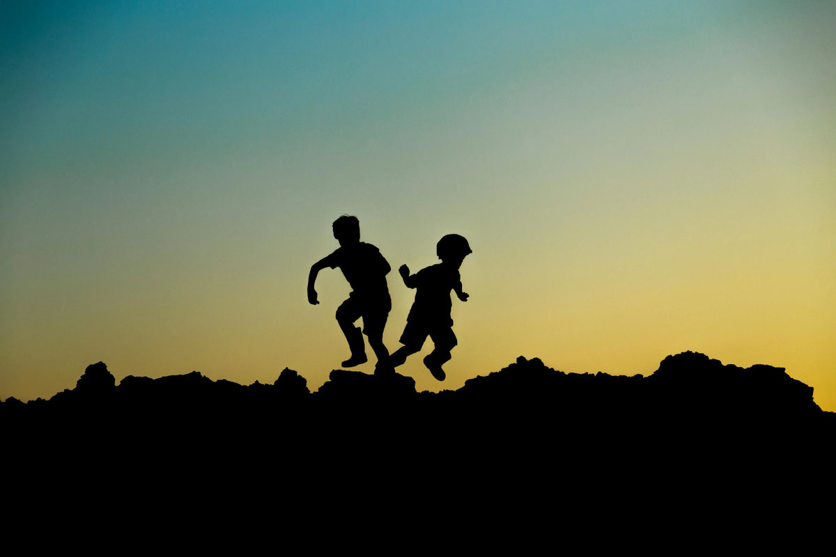 Silhouettes of two children jumping outdoors at sunset