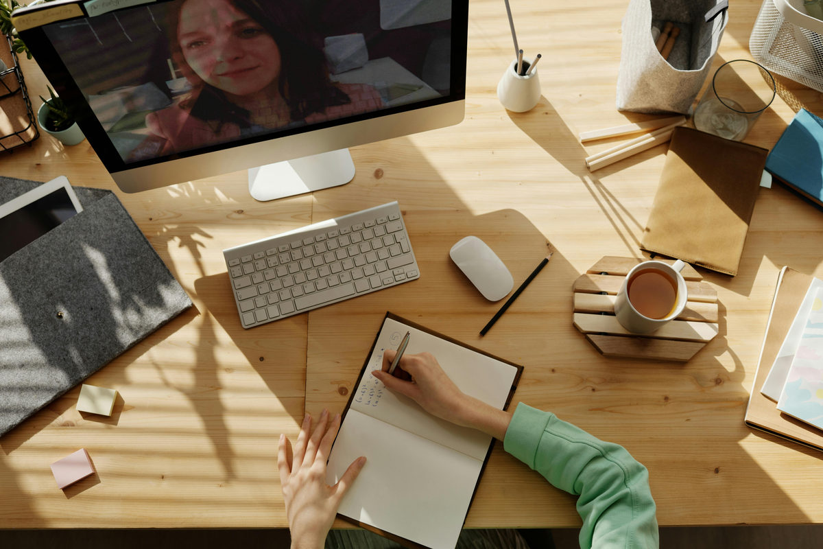 A video meeting on a computer beside a notebook.