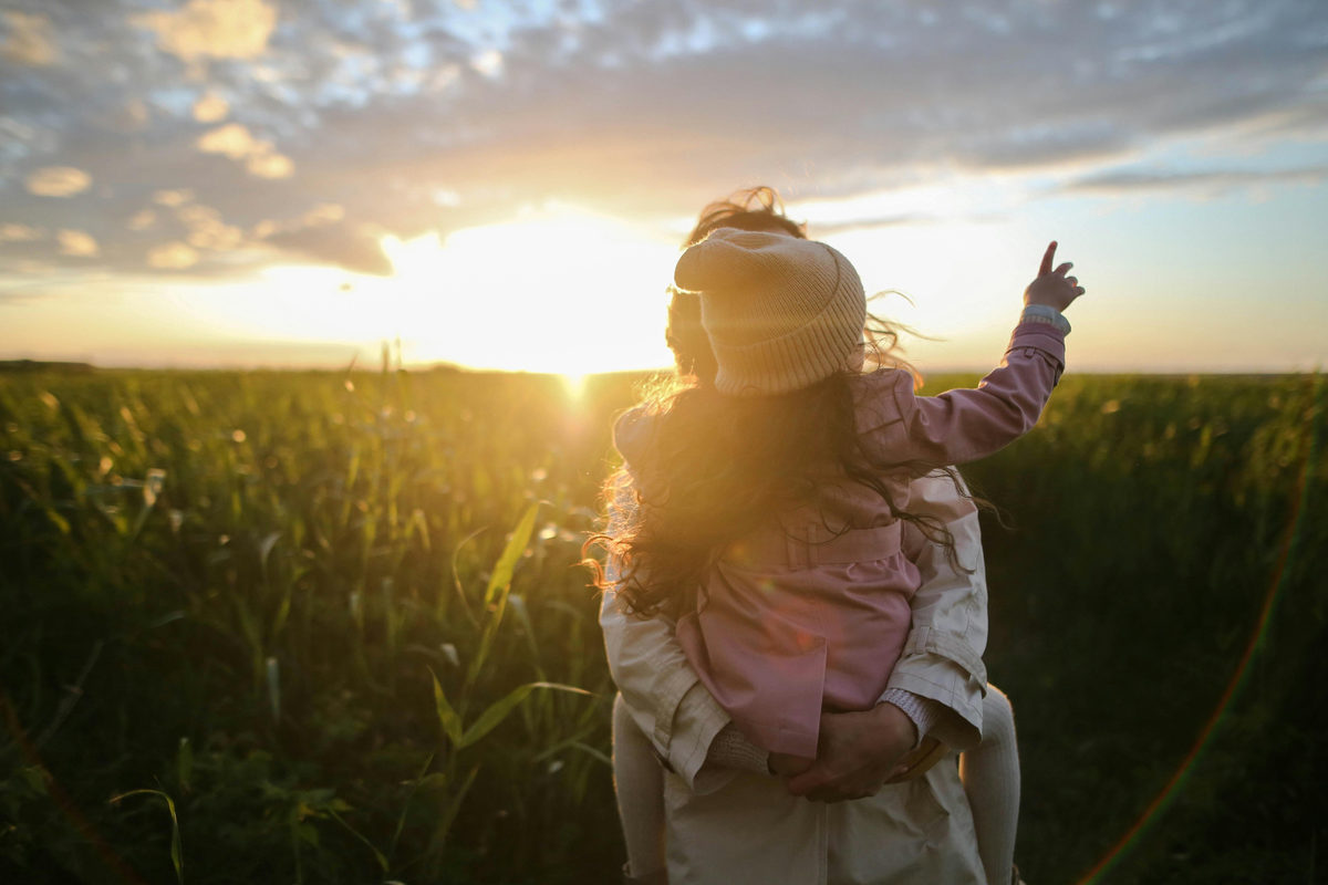 Adult holding a child in a field at sunset
