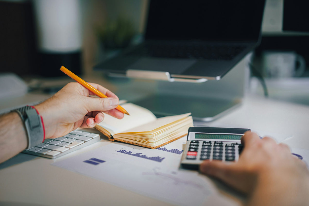 Hands using a calculator beside papers and a notebook.