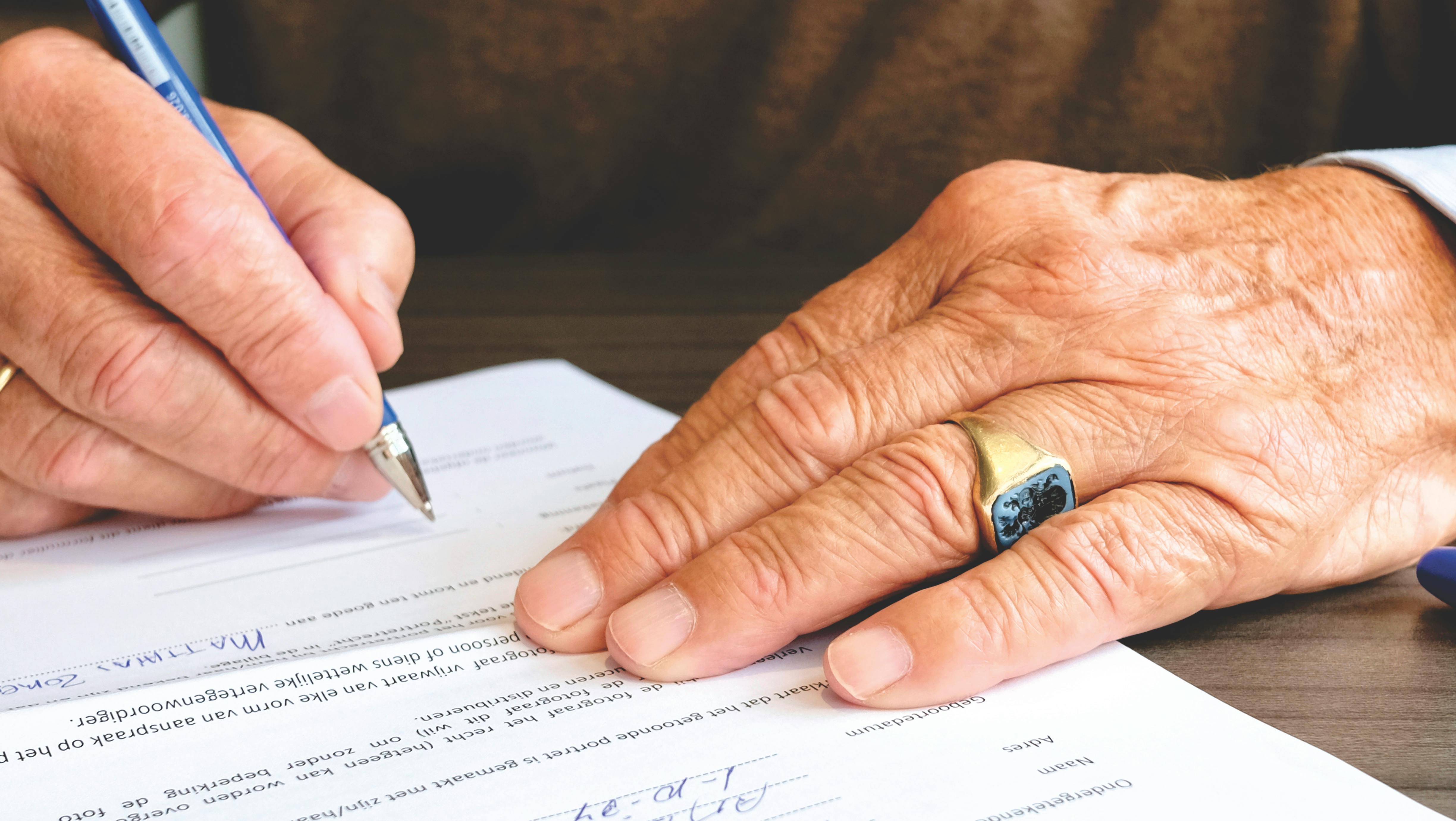 Close-up of a person signing a document with a blue pen.